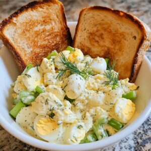 Creamy egg salad with celery, dill, and chives in a white bowl